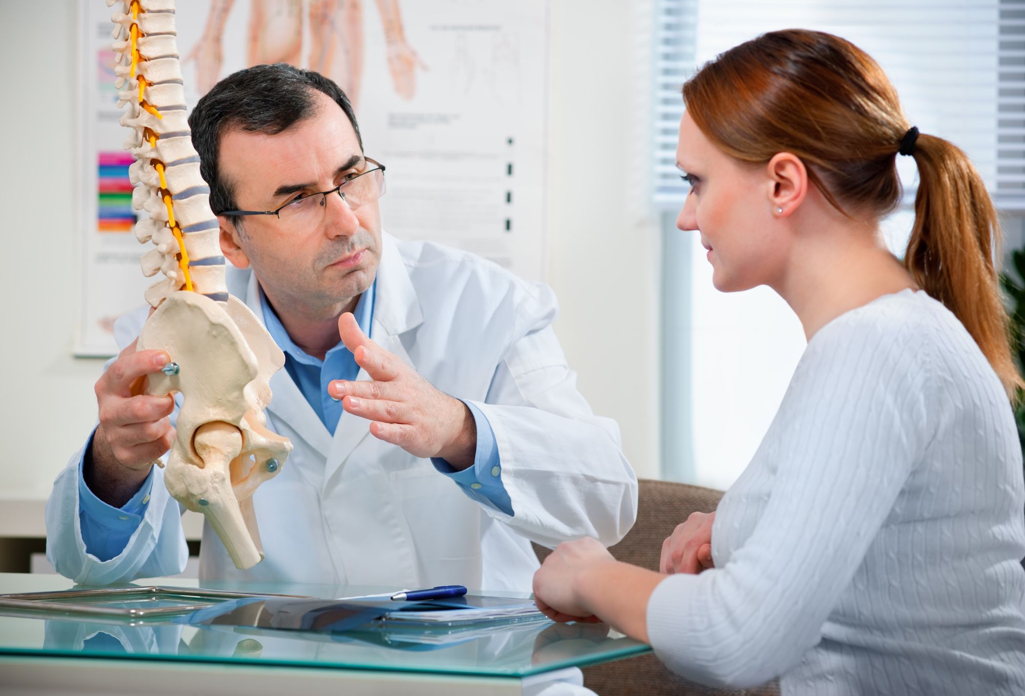 A Chiropractor shows the problem areas on the model of the spine to the patient and explains the cause of her pain.